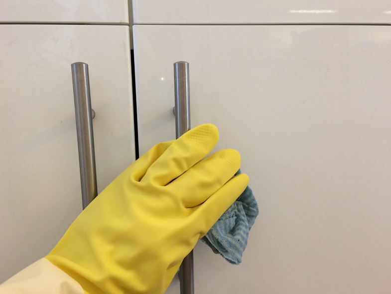  Wearing yellow cleaning gloves and wiping down the kitchen cupboards and handles. 